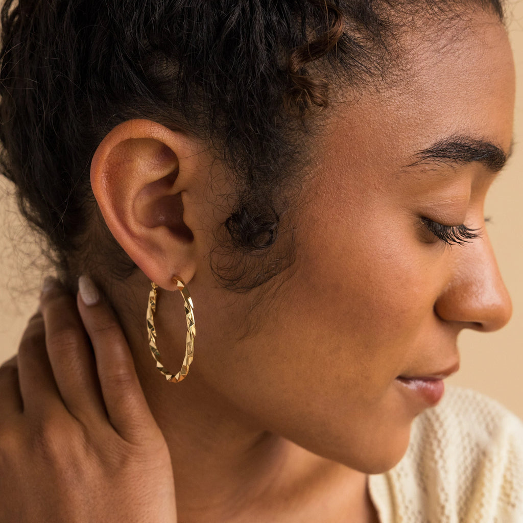 Woman with curly hair wears our Large Twisted Hoops, gently touching her neck in soft natural light—the perfect summer accessory for an effortlessly stylish look.