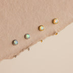 Two silver and two gold Opal Threader Huggies are displayed on a textured beige surface—an elegant set perfect for lovers of celestial jewelry and opal earrings.
