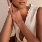Woman in a sleeveless cream top wears the Multiple Baguette Birthstone Bracelet and a gold ring with pink stones, hands clasped near her face.