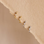 Four opal and diamond huggie earrings—two in gold and two in silver—neatly arranged on a textured beige background, highlighting the subtle sparkle and craftsmanship of each piece.