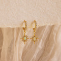 The Pave Opal Star Huggies capture celestial charm with gem-studded starburst pendants, beautifully showcased on a textured fabric background.