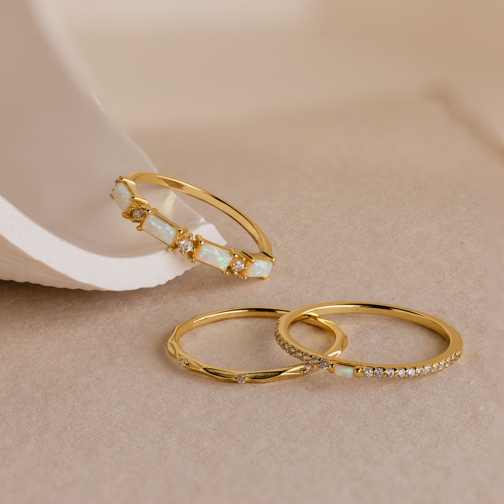 The Pave Opal Ring Set—featuring one opal pave ring and two rings with small diamonds—is displayed on a beige surface, highlighting its timeless design.