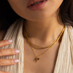 A woman wears layered gold necklaces, including the Labradorite & Moonstone Drop Necklace, with a cream textured top and her hand near her collarbone.