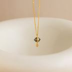 The Labradorite & Moonstone Drop Necklace features a shimmering gemstone pendant, suspended above a smooth, light-colored curved surface.
