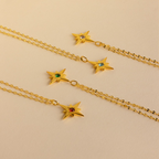 The Star Birthstone Necklace features four gold star pendants with colored gemstones on a beige background, making it a perfect piece of celestial jewelry or a personalized gift.