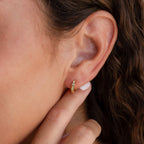 Close-up of a woman's ear adorned with Opal Inlay Diamond Huggies, featuring a delicate gold hoop as her hand gently touches her earlobe.