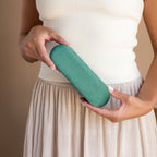 A woman wearing a white top displays the Slim Velvet Ring Box in green against her beige pleated skirt.