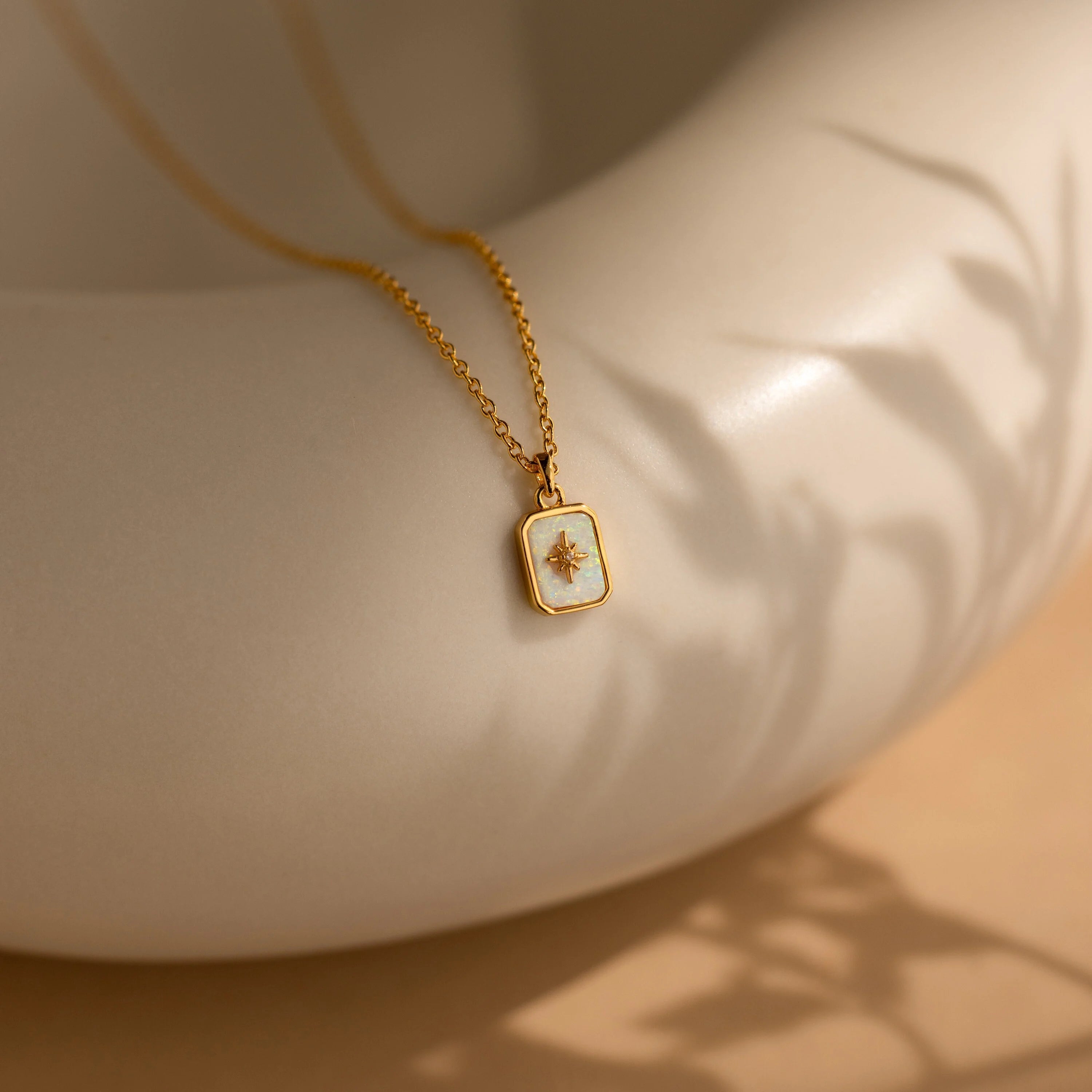 Opal North Star Birthstone Necklace for October featuring a diamond-set starburst design, displayed on a smooth beige ceramic surface with soft shadows.