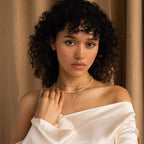 Woman with curly hair, in an off-shoulder white top, stands against a beige curtain wearing the Pearl & Diamond Duo Necklace.