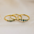The Lace Birthstone Rings Set features three delicate rings with small blue gemstones, displayed on soft beige fabric—a perfect personalized gift for lovers of minimalist jewelry.