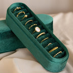The Slim Velvet Ring Box, featuring ten assorted gold rings, is displayed elegantly on a cream-colored fabric background.