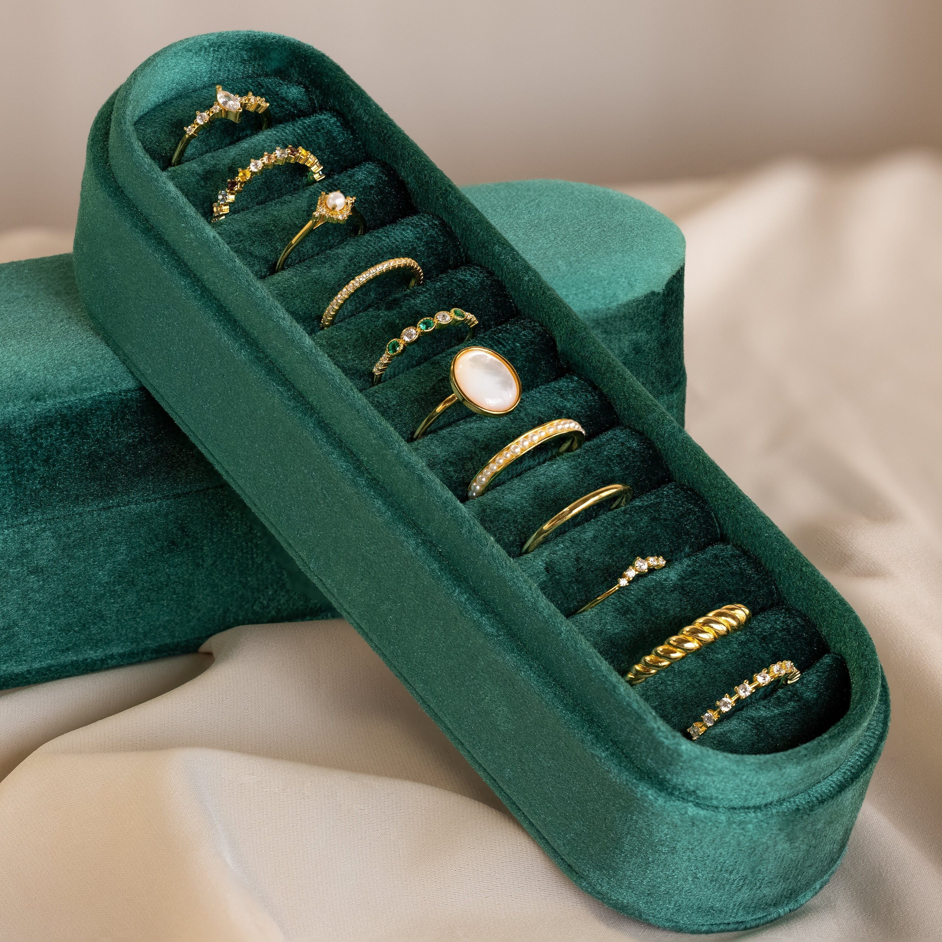 The Slim Velvet Ring Box, featuring ten assorted gold rings, is displayed elegantly on a cream-colored fabric background.