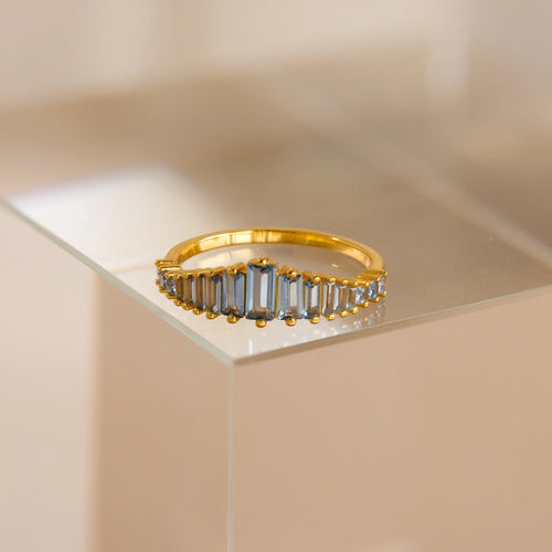 The Art Deco Aquamarine Ring features rectangular, light blue gemstones and is displayed on a clear surface, radiating vintage glamour.