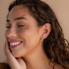 A woman with her eyes closed wears Ombre Opal Huggies, their gentle shimmer accentuating her serene beauty.