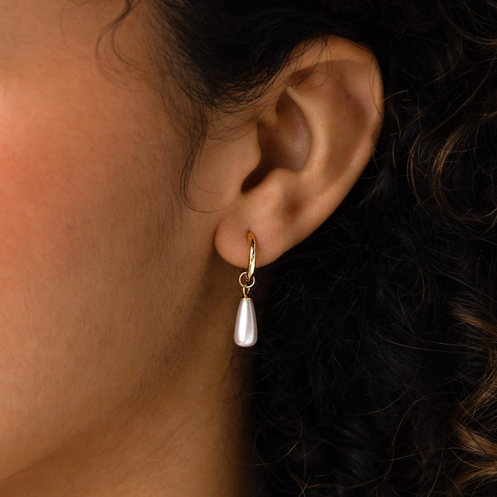 A close-up of an ear wearing Pearl Teardrop Huggies—gold hoop earrings with dangling pearl teardrops, ideal for bridal looks or a chic beach wedding.