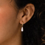 A close-up of an ear wearing Pearl Teardrop Huggies—gold hoop earrings with dangling pearl teardrops, ideal for bridal looks or a chic beach wedding.