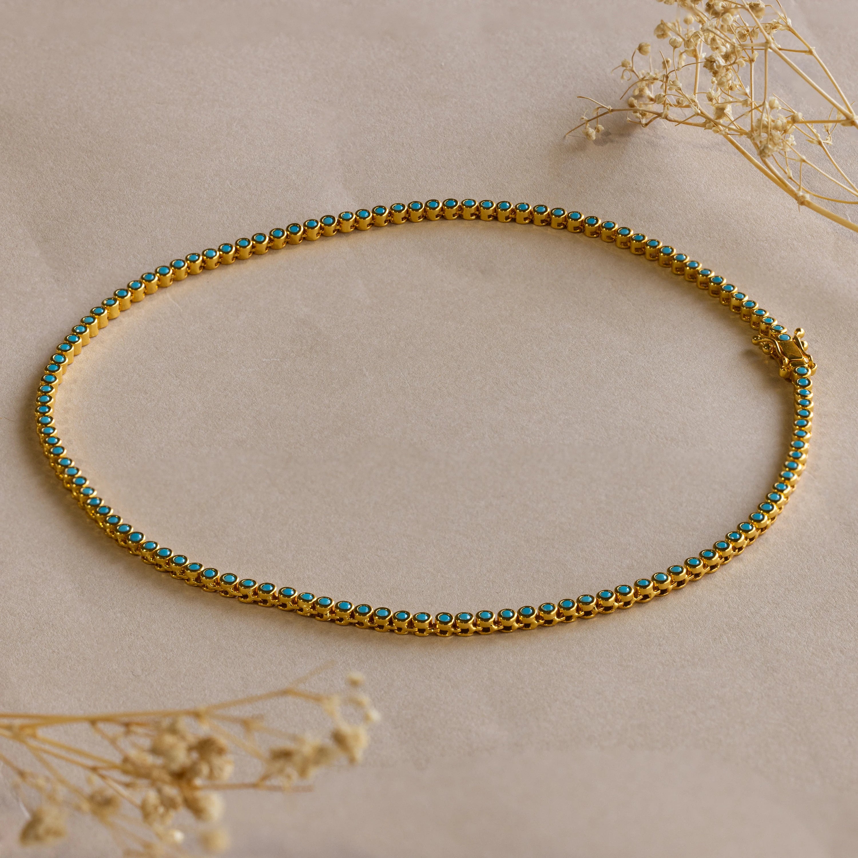 Gold anklet with turquoise stones, shown on a beige surface with dried flowers—pairs perfectly with our Turquoise Bezel Tennis Necklace for a coordinated look.