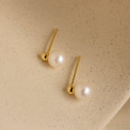 Classic Pearl Studs displayed on a textured beige surface, perfect for those who appreciate dainty earrings with timeless elegance.