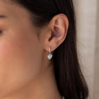 Close-up of a woman's ear wearing Pave Heart Drop Huggies—silver, heart-shaped huggie earrings adorned with sparkling gemstones, perfect as a romantic gift.