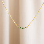 The Lace Birthstone Necklace features a gold chain with five small green beads, shown on a neutral light background—a delicate birthstone necklace ideal for everyday elegance.