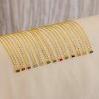 The Tapered Baguette Birthstone Necklace—a delicate gold mirror chain with a colorful rectangular gemstone pendant—is arranged neatly on a cream cloth.