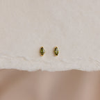 A pair of Marquise Birthstone Studs with personalized green marquise-cut gemstones, shown on textured white paper.