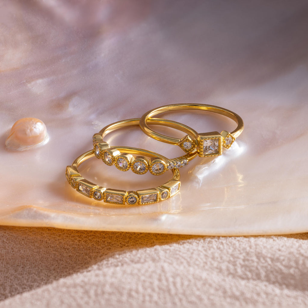 Three gold Art Deco rings with various diamond cuts displayed on a pearlescent shell surface.