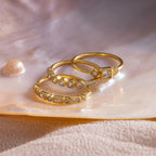 Three gold Art Deco rings with various diamond cuts displayed on a pearlescent shell surface.