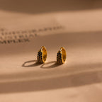 Chunky Onyx Pave Huggies—gold hoop earrings with black stones—cast bold shadows on a beige surface, blending modern style with classic elegance.