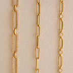 Three gold chain necklaces—a Pave Link Chain Necklace with sparkling diamonds, a plain chain, and one adorned with small round gems—are displayed on a neutral background.