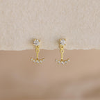 Round Diamond Ear Jackets in 18K Gold with brilliant-cut diamonds and delicate dangles are displayed on a textured cream surface.