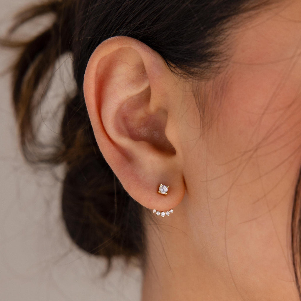Close-up of a woman's ear wearing the Round Diamond Ear Jackets, featuring a small diamond stud paired with a delicate arc design adorned with tiny crystals.