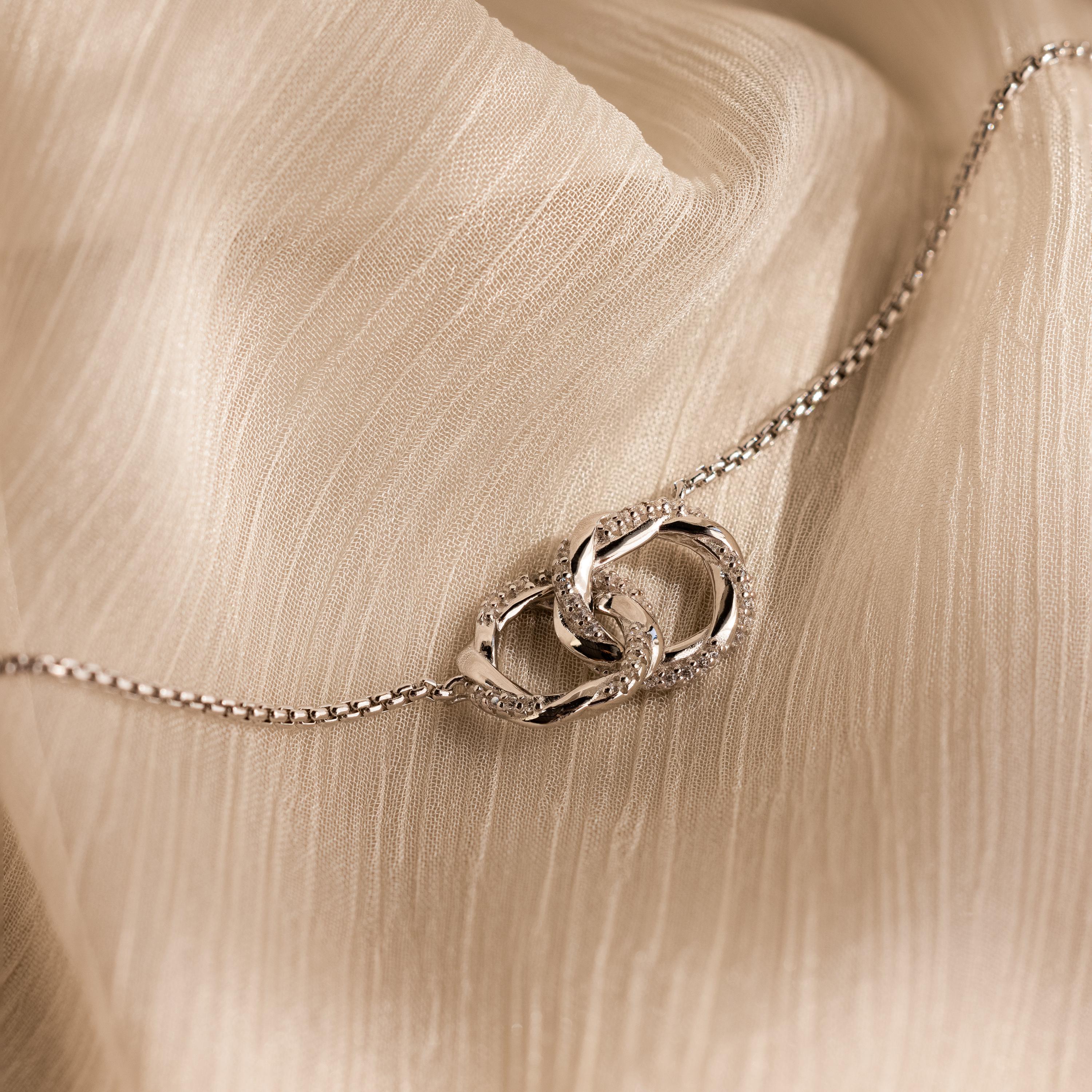Interlocking Pave Charm Necklace shown on textured beige fabric.