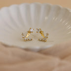 Diamond Cluster Ear Jackets featuring a front-back design and small sparkling stones are displayed on a white, scalloped dish—ideal for lovers of delicate earrings.