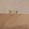Diamond Cluster Ear Jackets: Gold earrings with clear gemstones in a floral-inspired front-back design, shown on a textured beige surface.