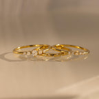 The Trio Diamond Stacking Ring Set, featuring delicate gold bands accented with small diamonds, rests on a smooth, reflective surface bathed in warm light.