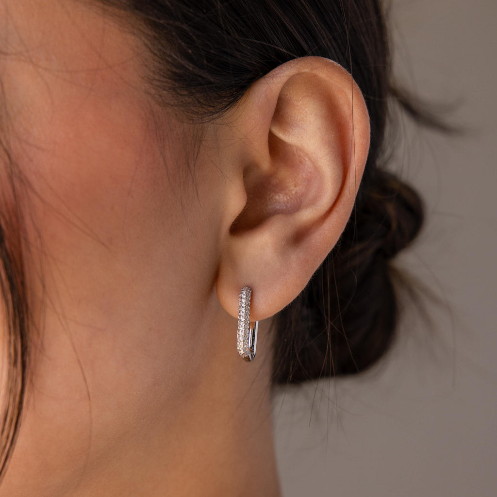 Close-up of a woman's ear adorned with Chunky Pave Link Earrings—sparkling pavé hoops encrusted with tiny diamonds, hair tied back.