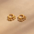 Chandelier Diamond Huggies—gold hoop earrings with dangling clear stones inspired by art deco elegance—displayed on a beige background.