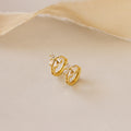 Close-up of Diamond Ribbon Bow Huggies in Gold set against a cream background.