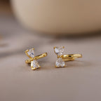 Diamond Bow Huggies featuring two clear, teardrop-shaped gems stacked vertically, displayed on a soft, neutral background.