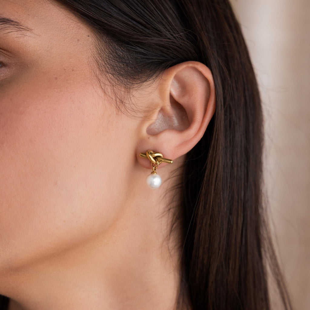 Close-up of a woman's ear wearing a Love Knot Pearl Earring with a dangling white pearl, perfect as an elegant wedding accessory.