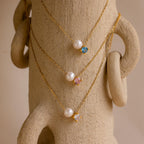 The Pearl & Birthstone Necklace, featuring pearls and colorful gemstones, is elegantly displayed draped over a textured beige sculpture.