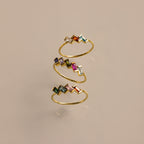 The Multiple Baguette Birthstone Ring is a gold spiral stackable ring with colorful rectangular gemstones, shown on a beige background.