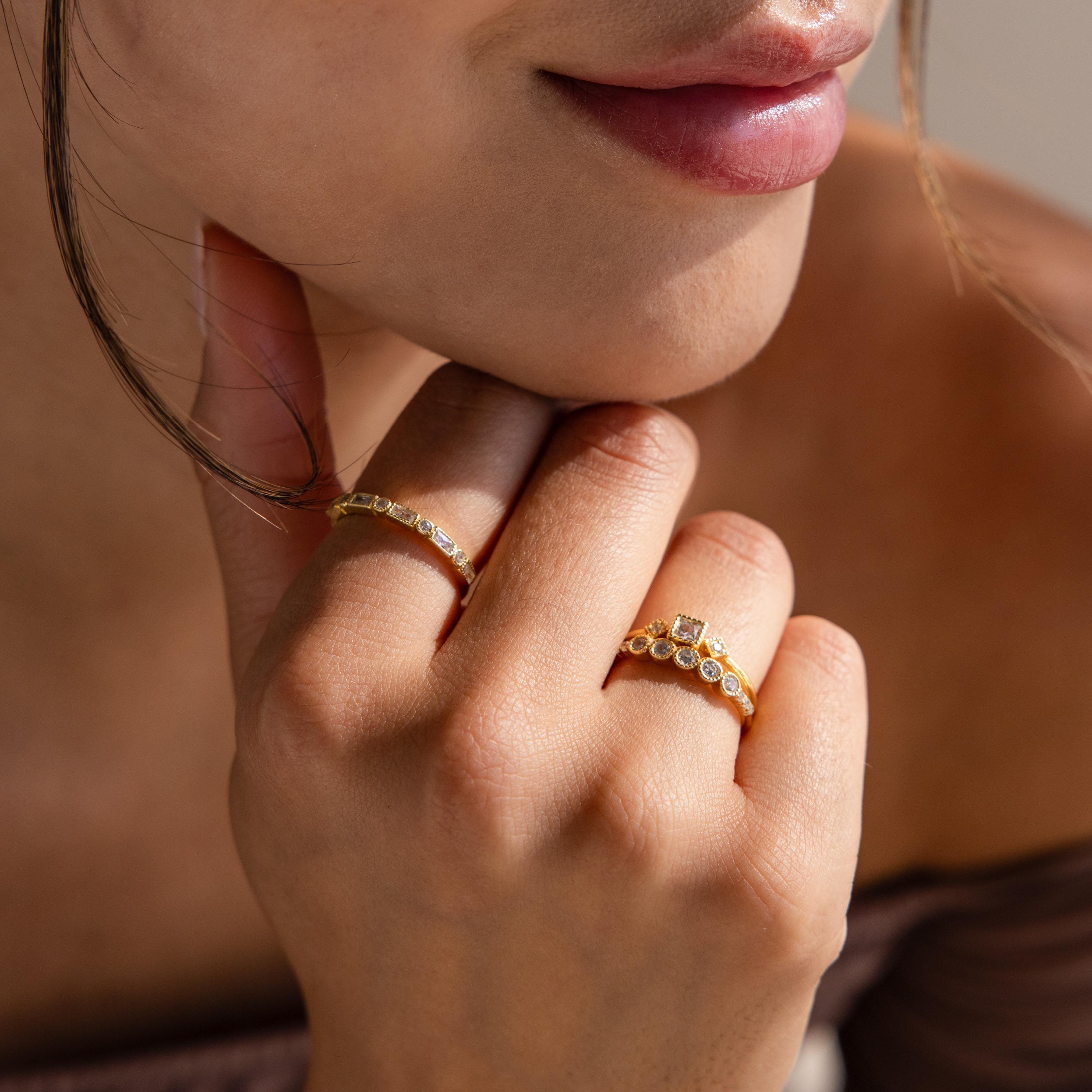 A woman rests her chin on her hand, smiling softly, while wearing the Art Deco Diamond Ring Set.