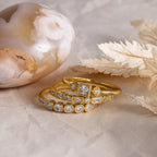 Stacked gold Art Deco diamond rings displayed on a textured surface beside a polished agate stone and dried leaves.