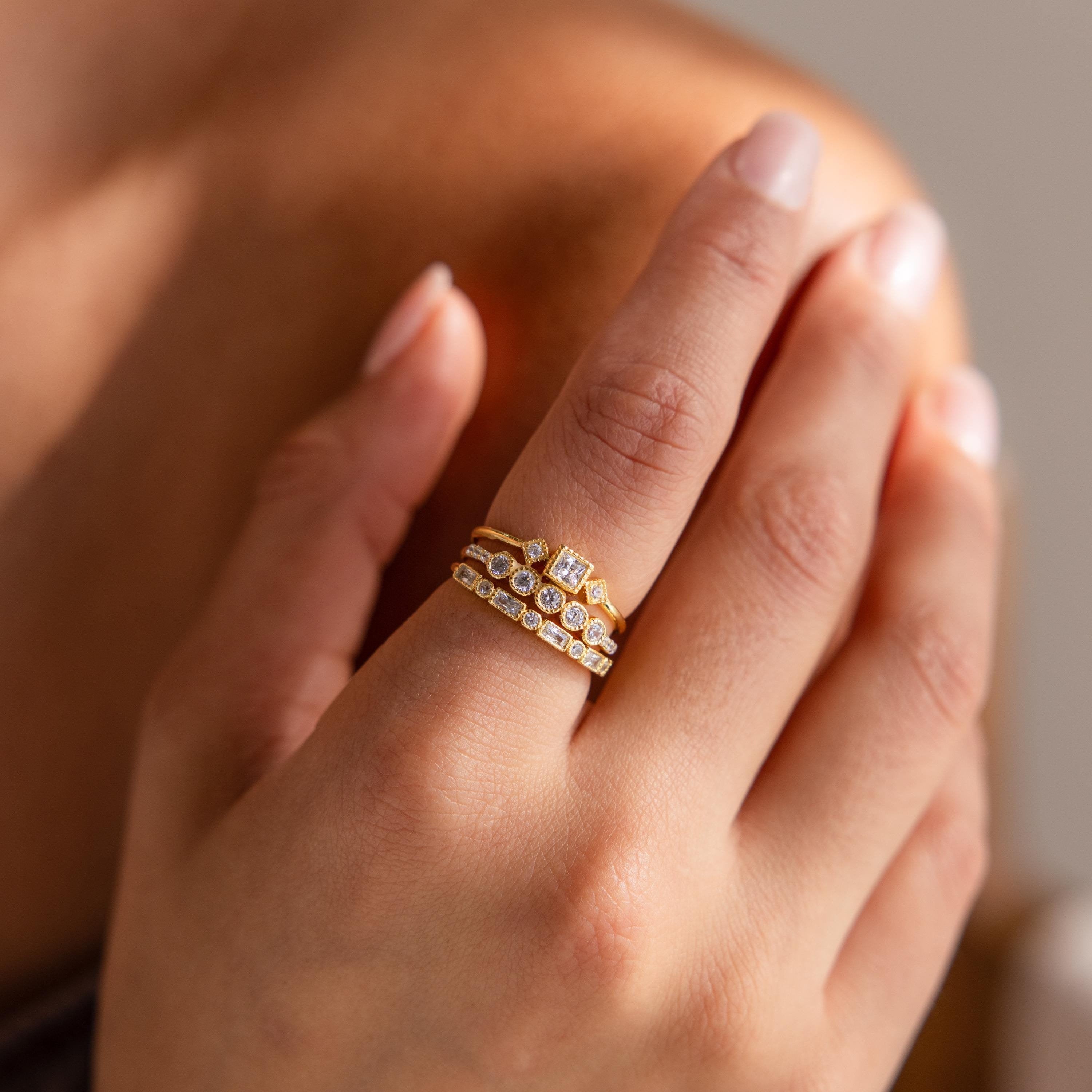 Hand wearing a stacked gold Art Deco diamond ring set with various cut stones, shown in soft natural lighting.