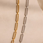 The Pave Link Chain Necklace is displayed on a textured beige surface with soft lighting, showcasing its rectangular gold and silver links.
