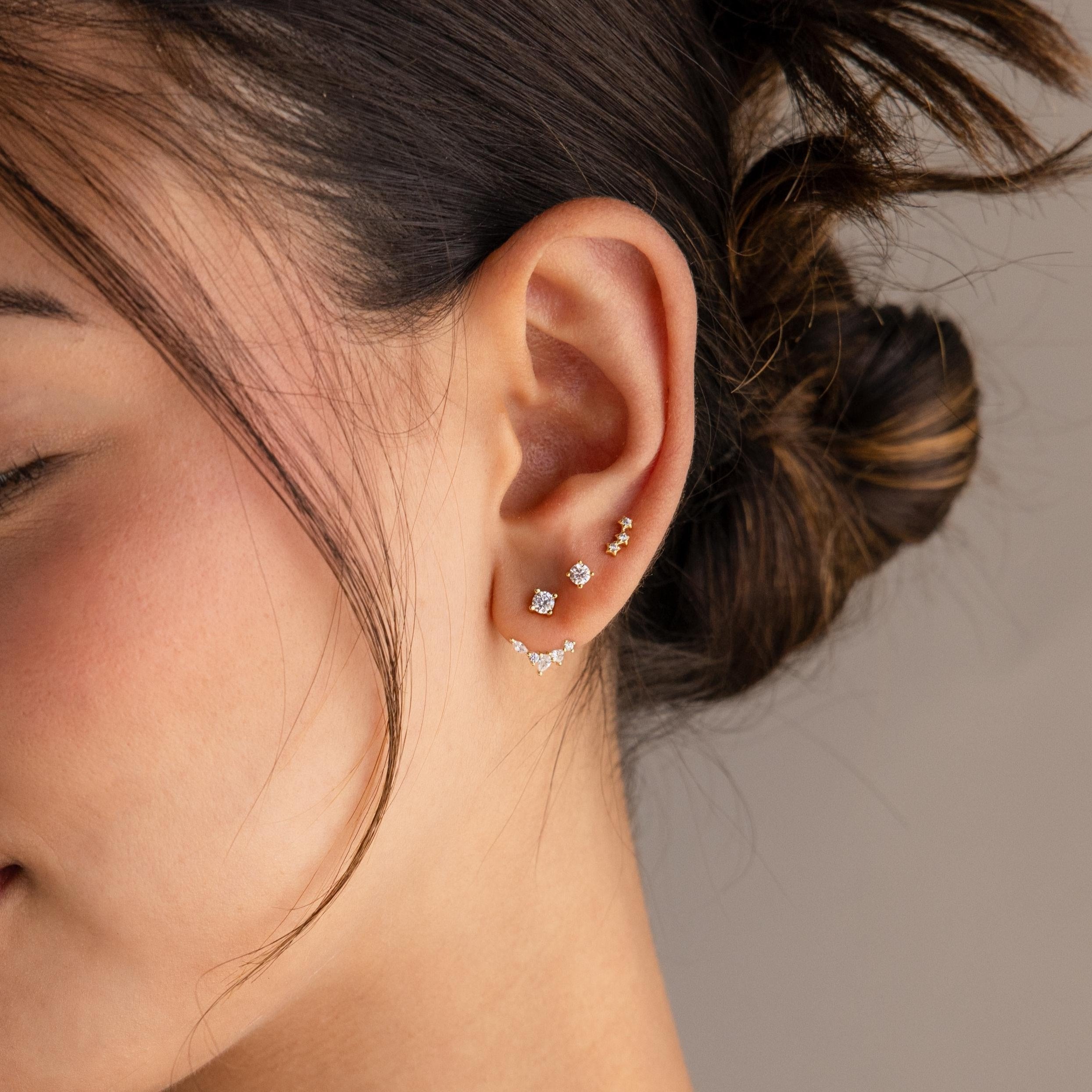 Close-up of a woman’s ear adorned with delicate gold and diamond studs, wearing Diamond Cluster Ear Jackets in a front back design, her hair tied back.