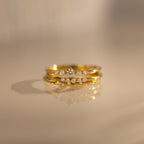 The Trio Diamond Stacking Ring Set, featuring three gold diamond rings including an art deco style, is elegantly stacked and reflected on a smooth beige surface.