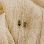 Two pairs of Toi et Moi Birthstone Studs in blue and gold rest on textured cream fabric—ideal as a custom gift or to add a personalized touch to your jewelry collection.
